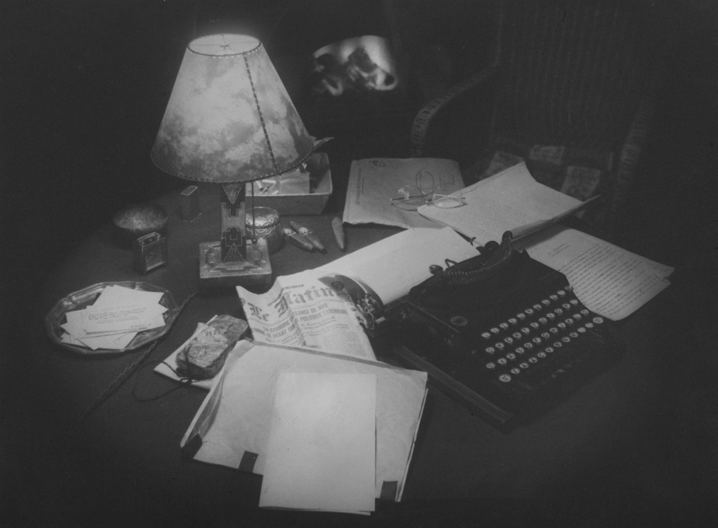 Macchina da scrivere antica su una scrivania disordinata con carte e una lampada.