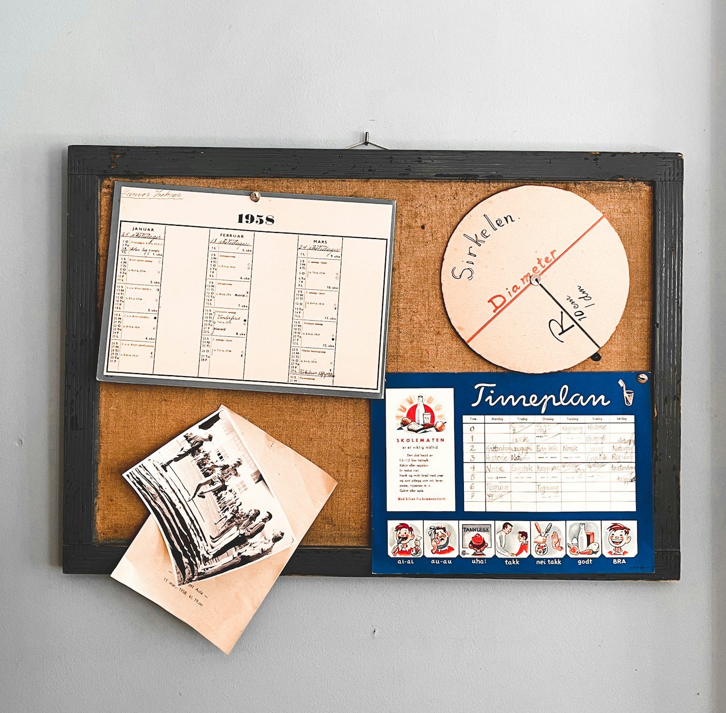Bacheca vintage in sughero con carte storiche e fotografie appese a un muro.