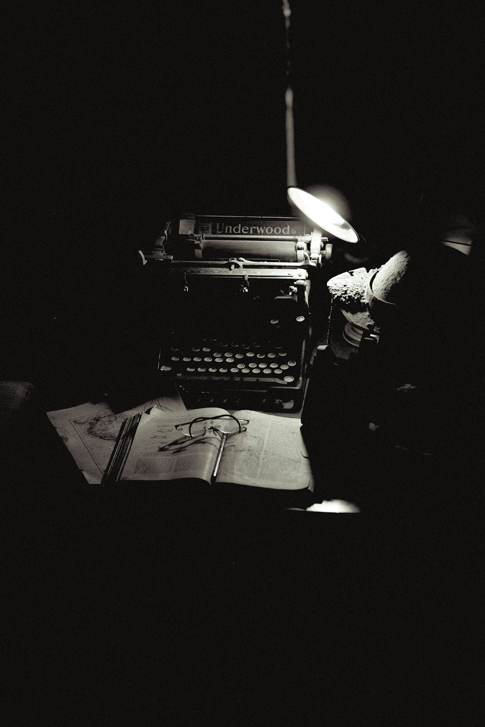 Macchina da scrivere vintage con libro aperto e occhiali su una scrivania.